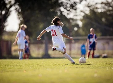Jente sparker fotball på en fotballbane